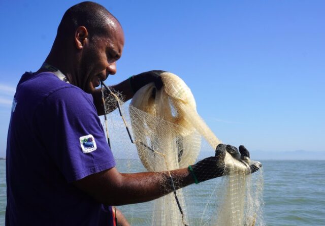 Imagem mostra pescador arrumando redes de pesca com as mãos