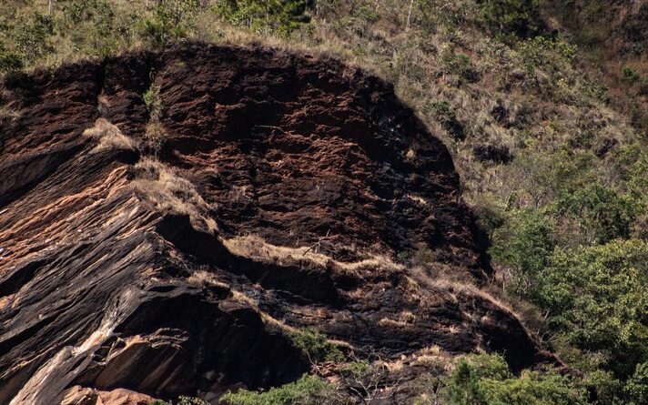 Imagem mostra terreno com formação rochosa em evidência e vegetação em volta