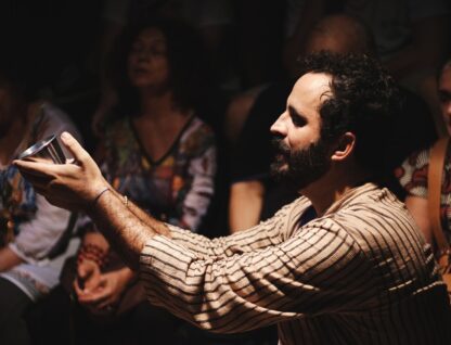 Imagem mostra cena de 'A paixão de Tito', na qual personagem ergue as mãos com recipiente metálico, como se estivesse pedindo algo