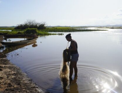 Foto mostra pescadora em Lagoa Feia, com os pés na água e uma rede nas mãos