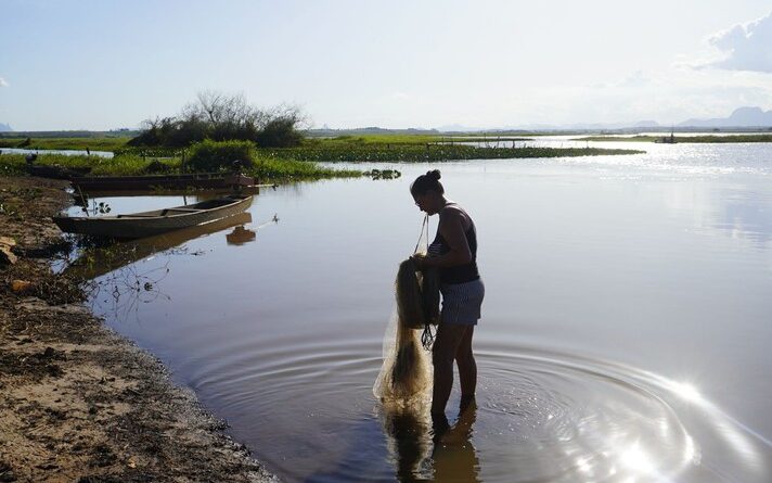 Foto mostra pescadora em Lagoa Feia, com os pés na água e uma rede nas mãos