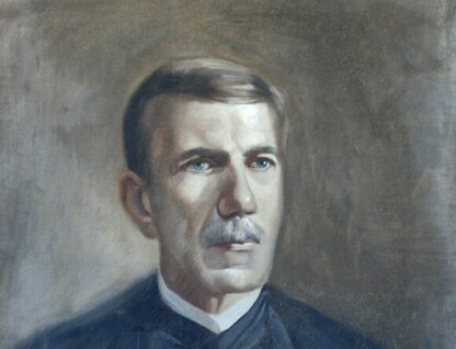 A imagem é uma pintura que retrata o busto de um homem com olhos azuis. Ele tem cabelos curtos e castanhos, e um bigode da mesma cor. O homem está com uma expressão séria, e veste uma roupa formal escura, com uma camisa branca de colarinho alto. O fundo da pintura é de um tom neutro, com pinceladas que variam entre marrom, cinza e bege.
