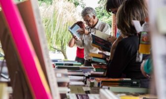 Imagem mostra livro em primeiro plano e, ao fundo, pessoas vendo outros livros em uma feira