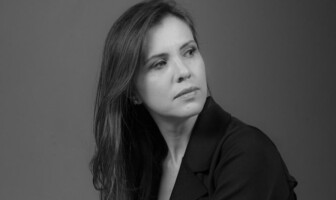 Foto em preto e branco. Carla Pedrosa, vestida com uma blazer preto, olha para o lado.