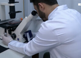 Pesquisador com jaleco olha pelas lentes de um microscópio