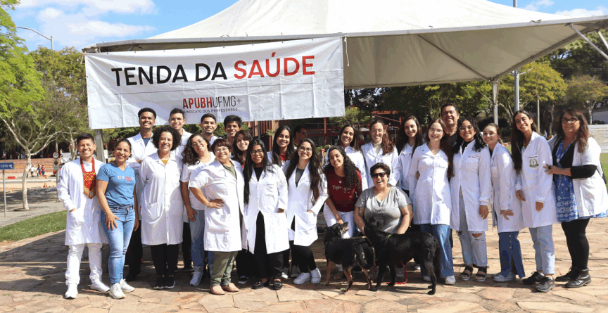 Grupo de professores e estudantes, em sua maioria vestidos com jalecos brancos, em frente a uma faixa onde se lê 'Tenda da Saúde'