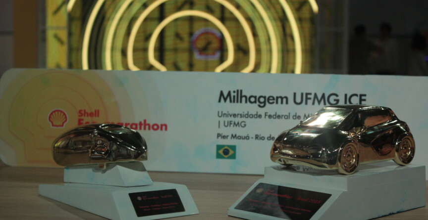 Dois troféus dourados no formato de prótipos de carros sobre uma base branca. Ao fundo, encontra-se placa de premiação com a inscrição Milhagem UFMG ICE ao lado da logo da Shell 