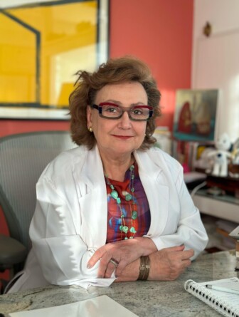 Margareth Dalcolmo é uma mulher branca com óculos. Nesta foto, ela usa um casaco branco e uma blusa estampada