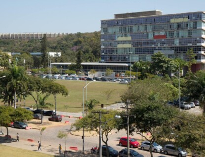 Imagem mostra o prédio da Reitoria, tendo à frente uma área verde e trecho da principal avenida do campus Pampulha, a Mendes Pimentel