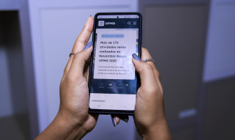 Usuária segura com as duas mãos um celular que exibe conteúdo novo portal da UFMG