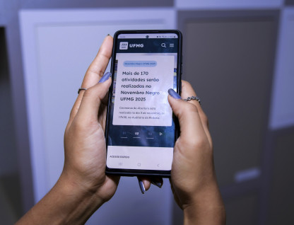 Usuária segura com as duas mãos um celular que exibe conteúdo novo portal da UFMG