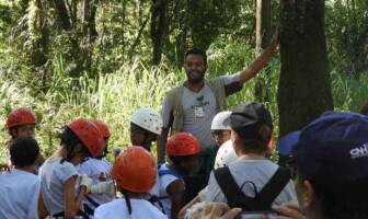 Instrutor conversa com crianças em área arborizada