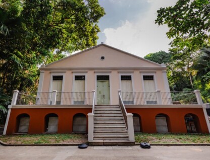 Prédio em tons rosa construído em área arborizada