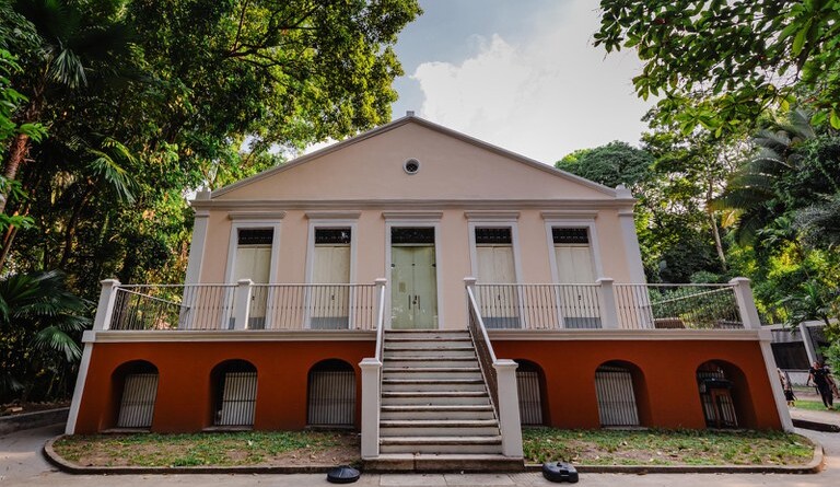 Prédio em tons rosa construído em área arborizada