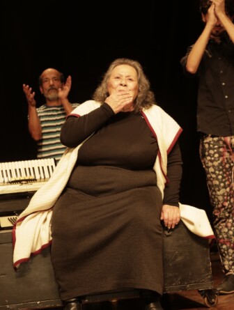 Teuda Bara com a mão na boca, mandando um beijo para a plateia, durante espetáculo 'De tempos somos', encenado na UFMG