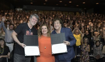 Wilson Lopes, reitora Sandra e Toninho Horta seguram diplomas em cima do palco, na frente da plateia