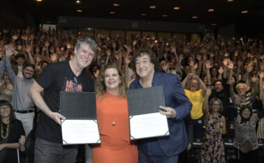 Wilson Lopes, reitora Sandra e Toninho Horta seguram diplomas em cima do palco, na frente da plateia