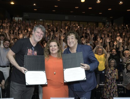 Wilson Lopes, reitora Sandra e Toninho Horta seguram diplomas em cima do palco, na frente da plateia