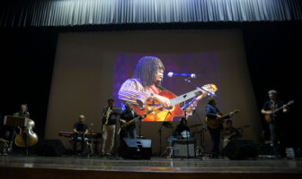 No auditório da UFMG, músicos realizam apresentação em tributo aos membros do Clube da Esquina, com imagem de Milton Nascimento ao fundo