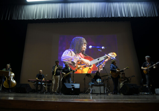 No auditório da UFMG, músicos realizam apresentação em tributo aos membros do Clube da Esquina, com imagem de Milton Nascimento ao fundo