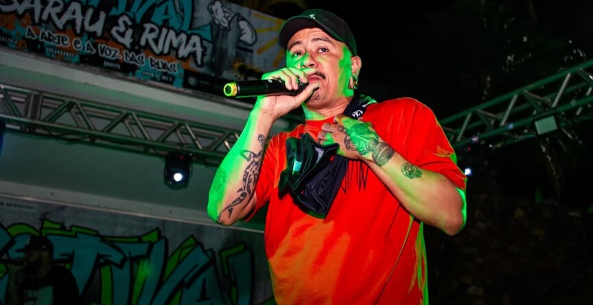 Slammer João Paiva no palco, com camisa vermelha e microfone na mão, recitando poesia