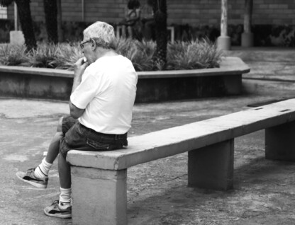 Homem idoso de camisa branco sentado em um banco de praça pública