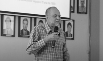 Valdir de Castro Oliveira, professor aposentado da Fafich, com microfone na mão, sobre um palco