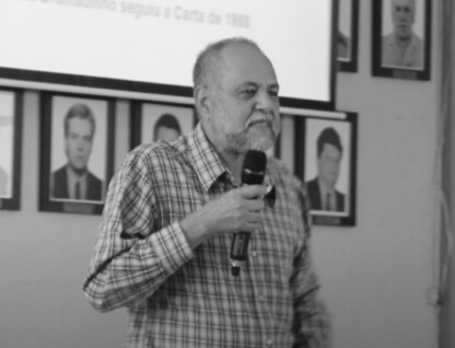 Valdir de Castro Oliveira, professor aposentado da Fafich, com microfone na mão, sobre um palco