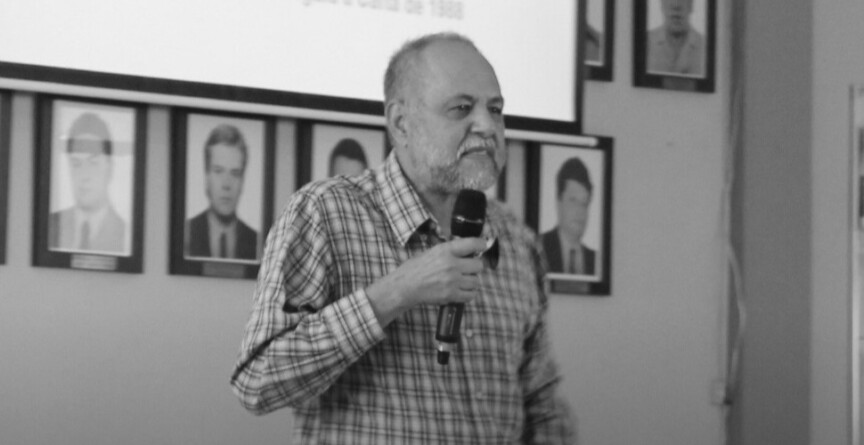 Valdir de Castro Oliveira, professor aposentado da Fafich, com microfone na mão, sobre um palco