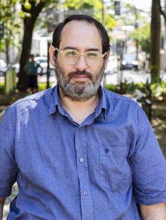 Foto do pesquisador Pedro Kalil usando óculos e vestindo uma camisa azul de botões