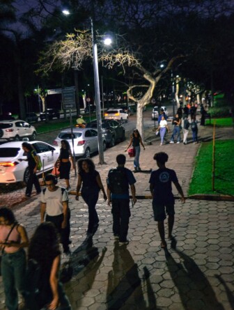 Alunos transitam pelo campus Pampulha à noite, iluminados por luz artificial