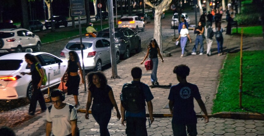 Alunos transitam pelo campus Pampulha à noite, iluminados por luz artificial