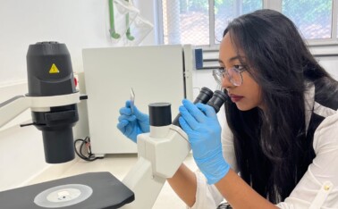Pesquisadora Nathalia Oliveira, da Faculdade de Farmácia, manipula lâminas de vidro junto a um microscópio