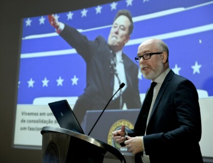 Vladimir Safatle fala para o público o auditório da reitoria. Ao fundo, uma imagem do magnata Elon Musk, dono do X