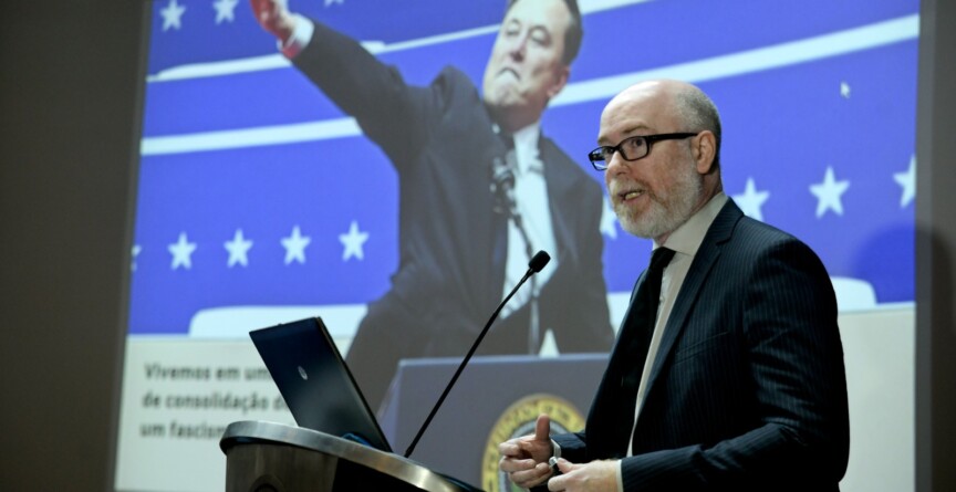 Vladimir Safatle fala para o público o auditório da reitoria. Ao fundo, uma imagem do magnata Elon Musk, dono do X