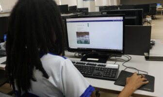 Mulher de cabelos pretos e roupa branca está diante de uma tela de computador que exibe informações sobre livro eletrônico