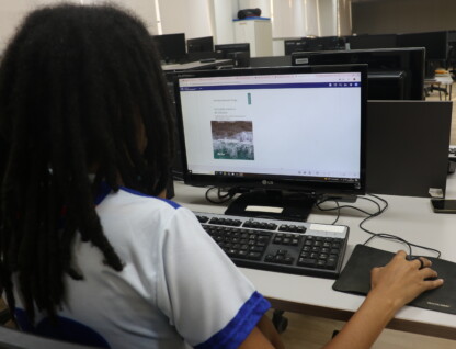 Mulher de cabelos pretos e roupa branca está diante de uma tela de computador que exibe informações sobre livro eletrônico