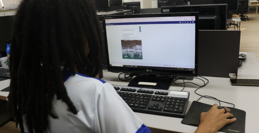 Mulher de cabelos pretos e roupa branca está diante de uma tela de computador que exibe informações sobre livro eletrônico