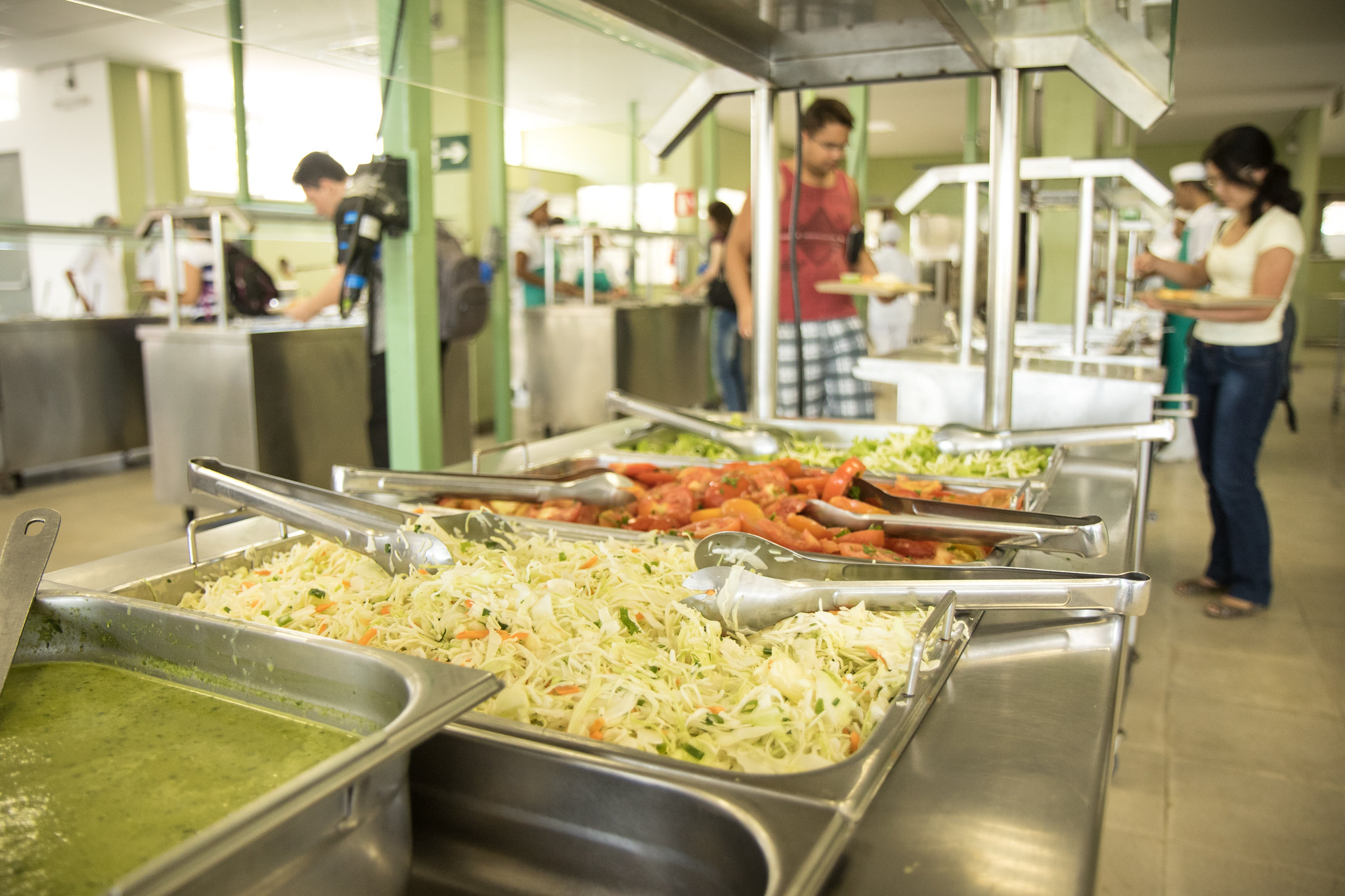 Vegetais à disposição dos estudantes para se servirem, ao fundo, estudantes já se servindo