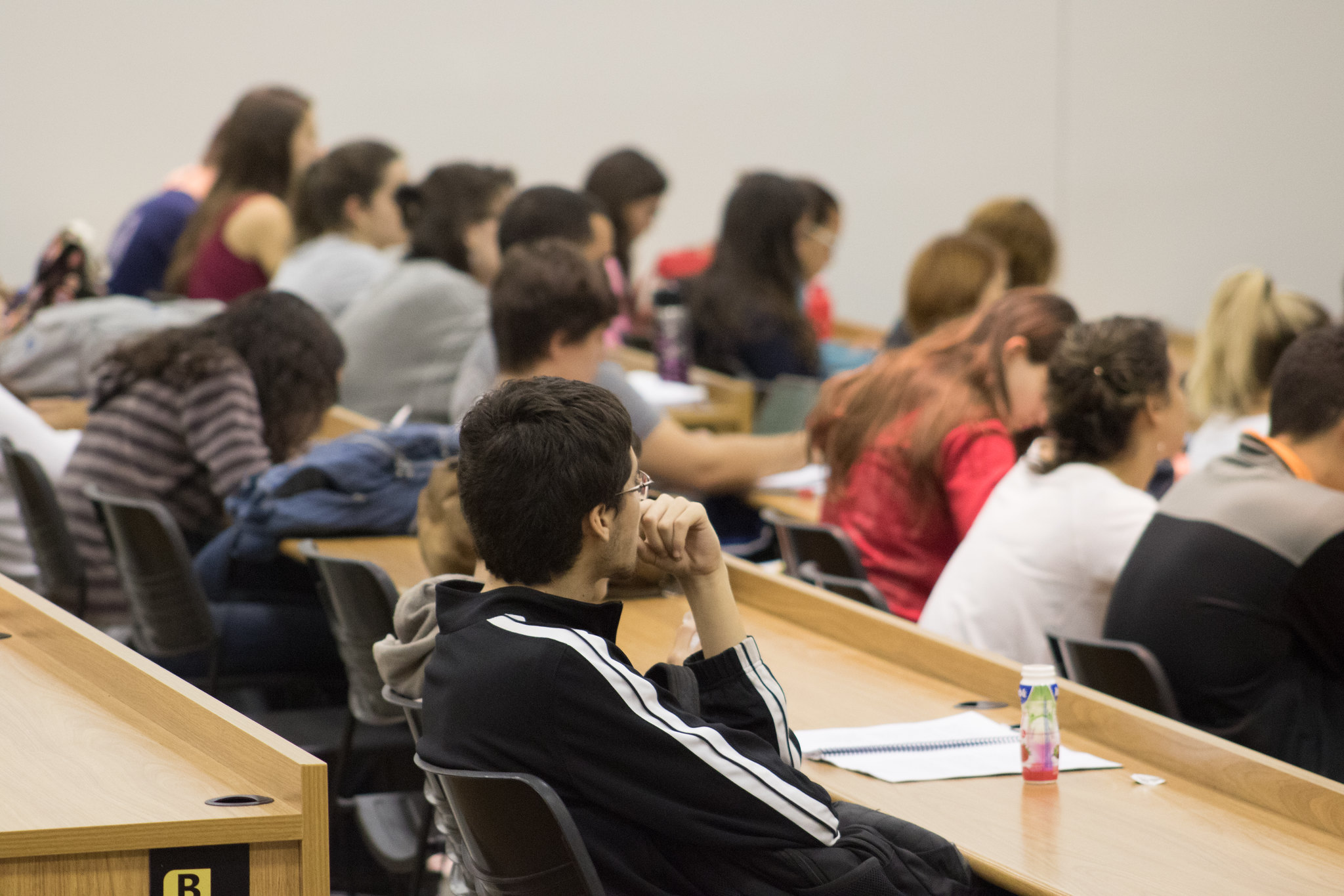 Auditório da faculdade de Medicina durante aula de microbiologia. Ao centro, aluno com a mão no queixo e, ao fundo, alunos fazendo anotações.