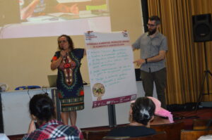 Cursista Elza, auxiliada pelo Prof. Thiago Canettieri, apresentou a síntese das discussões realizadas durante uma atividade em grupo na qual os cursistas, com base nos temas da 2ª edição do Curso de Formação, propuseram políticas públicas e ações concretas / Foto: Clarissa Veloso